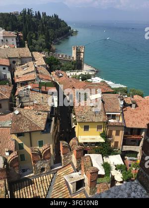 High-angle view of the historic center of Sirmione with terracotta roofs, looking over the medieval town walls toward the blue waters of Lake Garda. Stock Photo