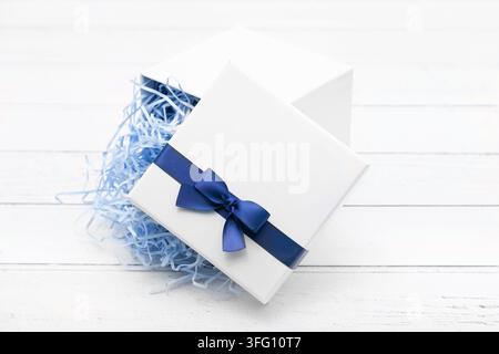 Elegant white gift box opened with gold ribbon bow and beige shredded paper filler on a white wooden background, perfect for luxury packaging. Stock Photo
