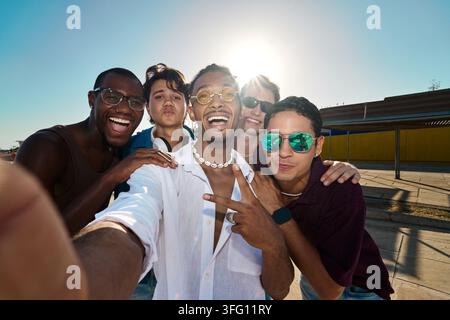 Happy group of young diverse men smiling and laughing while taking a selfie together on a sunny summer day. Celebrating friendship and diversity Stock Photo