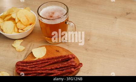 Large beer mug with fried sausages. Beer and snack. Beer, Grilled sausage, potato chips on bar table. Beer pub set. Stock Photo