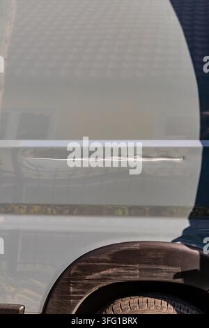 Close-up of scratches, scuff marks and a long dent on the side panel and wheel arch of a work van. Stock Photo