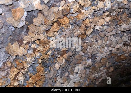 Close-up abstract background texture of a rough, bumpy volcanic rock wall featuring natural shades of brown, ochre, grey, and black. Southport, UK. Stock Photo