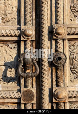 Ornately carved wooden door with intricate patterns and a decorative handle, Ornamental door knocker on old carved wood panel door close up detail of Stock Photo