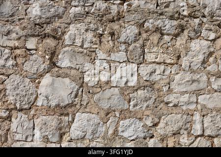 Rough limestone wall composed of irregular blocks and sandy mortar, showcasing weathered texture and rustic character. Ideal for architectural backgro Stock Photo