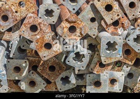 Close-up view of stacked rusted scaffolding base plates showing weathered metal, flaking corrosion and repeating geometric holes. Suitable for industr Stock Photo