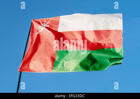 Flag of Oman. Flag waving in the wind against a clear blue sky, fluttering on a flagpole outdoors. Bright sunny day, fabric texture, outdoor close-up Stock Photo