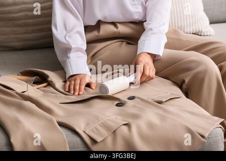 Personal grooming and garment care, woman using a lint roller to remove dust and pet hair from a beige blazer for a professional appearance Stock Photo
