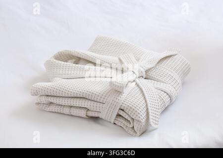 Folded waffle bathrobe on white blanket in bedroom Stock Photo