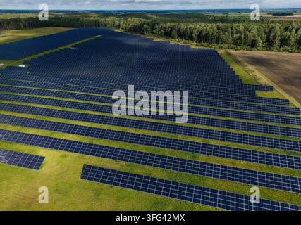 Aerial view of expansive solar farm across green countryside landscape bordered by forest and agricultural fields, large scale renewable energy and so Stock Photo