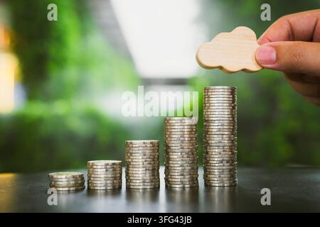 Cloud data storage cost and weather insurance concept with hand placing wooden icon on rising coin stacks on table against green bokeh background Stock Photo