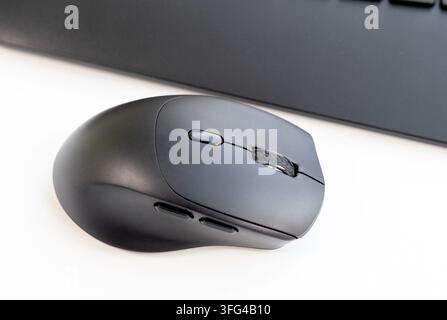 A sleek black computer mouse rests on a white desk near a keyboard Stock Photo