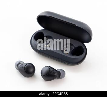 Black true wireless earbuds and their charging case are displayed on a white surface Stock Photo