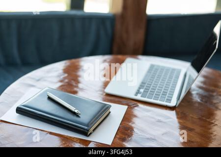 Laptop, notebook and pen on wooden table in modern workspace. Business planning, remote work, productivity and office technology concept. Stock Photo