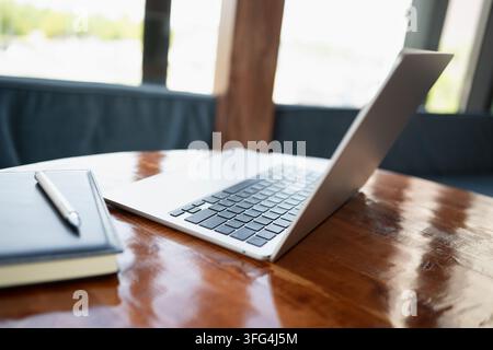 Open laptop and notebook on wooden table in modern interior with copy space. Remote work, digital office, productivity and business technology concept Stock Photo