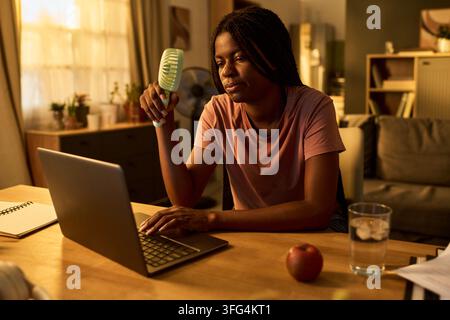 Black Woman Using Portable Fan While Working on Laptop at Home Stock Photo