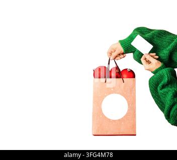 hand holding a holiday shopping bag with red Christmas ornaments and blank gift card, isolated on white background with large copy space, concept of r Stock Photo