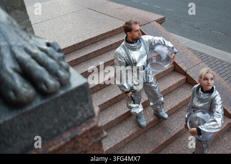 Astronauts take their helmets off on the steps of an old building. The air of the new planet turns out to be safe, and the explorers look around witho Stock Photo