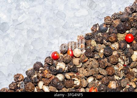Macro texture shot showing a diagonal split between coarse white rock sea salt crystals and mixed black, white, and red peppercorns. Stock Photo