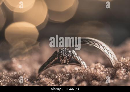 Macro shot of a diamond engagement ring and patterned wedding band resting on a brown textured sand like surface with a golden bokeh background. Stock Photo