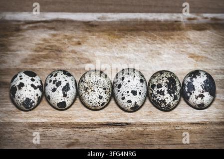 Six speckled quail eggs arranged in a neat horizontal row on a rustic wooden board, featuring large copy space at the top. Stock Photo