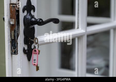 Key with a pink numbered tag hanging from a black vintage door handle on a white glazed entrance door. Concept of property access, keys, security, ide Stock Photo