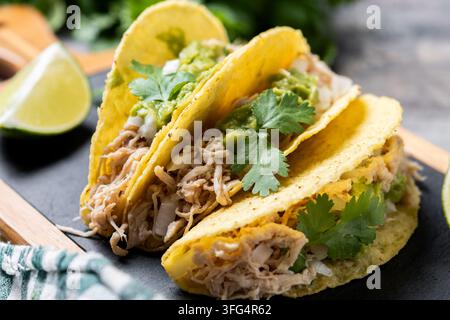 Close-up of crispy Mexican tacos filled with shredded chicken, guacamole, onion and fresh cilantro, served with lime wedges. Stock Photo