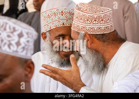 Close-up of two elderly Omani men wearing embroidered kuma caps laughing and gesturing together at the Nizwa market, Ad Dakhiliyah Region, Nizwa, Oman Stock Photo