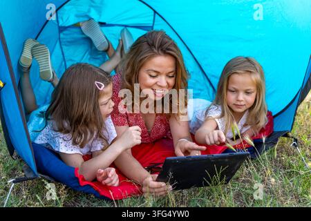 Family lying in a tent, bonding and using a tablet during leisure time outdoors Stock Photo