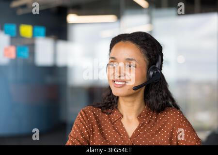 Young female call center agent wearing a headset and smiling, providing professional support and communication to clients in a modern office environment Stock Photo