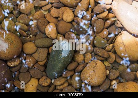 Full frame view of natural brown river pebbles resting underwater with bright light reflections creating a soothing textured pattern for spa wellness Stock Photo