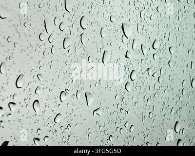 Close-up macro photo of water droplets and rain trails on a glass surface against a soft light background. Stock Photo