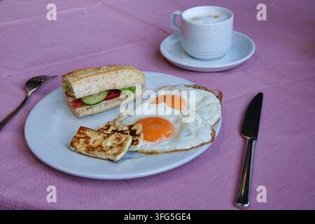 A healthy morning breakfast served on a pink tablecloth, featuring a white plate with two sunny-side-up fried eggs, grilled halloumi cheese slices, an Stock Photo