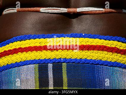Macro view of a striped beaded belt in blue yellow and red resting above a plaid skirt, Cunene Province, Cahama, Angola Stock Photo