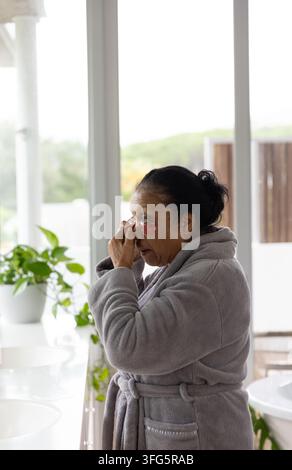Senior African American woman in gray robe applying pink hydrogel under-eye patches at vanity Stock Photo
