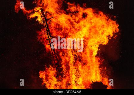 LADDER STRUCTURE IN THE INFERNO, BURNING THE WICKER MAN EFFIGY, GREEN MAN FESTIVAL, BRECON, WALES, UK, 2016: The dark silhouette of a wooden ladder-like structure is visible at the heart of a vast, raging fire of intense orange flames. Photo: Rob Watkins. INFO: The Green Man Festival is held annually in the Brecon Beacons in August. It celebrates music, arts, literature, science and family-friendly culture in a beautiful mountain setting. Each year the festival ends with the ritual burning of the wicker man Green Man effigy. Stock Photo
