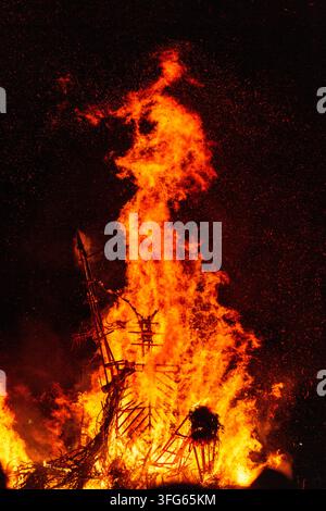 FACE-LIKE SHAPE FORMS IN A RAGING FIRE, BURNING THE WICKER MAN EFFIGY, GREEN MAN FESTIVAL, BRECON, WALES, UK, 2016: Intense orange flames from a burning boat effigy rise to form a strange, face-like shape against the dark, spark-filled night sky. Photo: Rob Watkins. INFO: The Green Man Festival is held annually in the Brecon Beacons in August. It celebrates music, arts, literature, science and family-friendly culture in a beautiful mountain setting. Each year the festival ends with the ritual burning of the wicker man Green Man effigy. Stock Photo