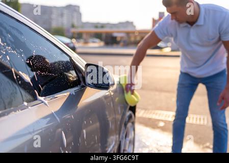 Man washes the gray vehicle using a large porous sponge Stock Photo