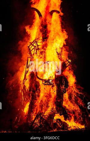 CLOSE UP OF A BURNING HORNED EFFIGY, BURNING THE WICKER MAN EFFIGY, GREEN MAN FESTIVAL, BRECON, WALES, UK, 2018: Intense flames engulf a large wooden effigy with horns, revealing the intricate stick structure within the heart of the roaring fire. Photo: Rob Watkins. INFO: The Green Man Festival is held annually in the Brecon Beacons in August. It celebrates music, arts, literature, science and family-friendly culture in a beautiful mountain setting. Each year the festival ends with the ritual burning of the wicker man Green Man effigy. Stock Photo