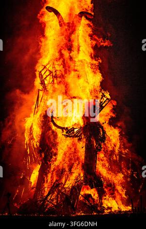 BURNING EFFIGY'S FACE GLOWS IN THE DARKNESS, BURNING THE WICKER MAN EFFIGY, GREEN MAN FESTIVAL, BRECON, WALES, UK, 2018: The face and horns of a large wooden effigy glow with intense heat as the structure is consumed by a towering inferno at night. Photo: Rob Watkins. INFO: The Green Man Festival is held annually in the Brecon Beacons in August. It celebrates music, arts, literature, science and family-friendly culture in a beautiful mountain setting. Each year the festival ends with the ritual burning of the wicker man Green Man effigy. Stock Photo