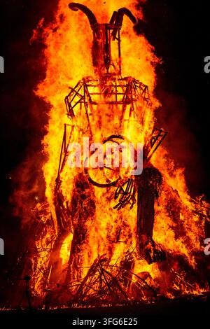 SILHOUETTED HORNED FIGURE IN A RAGING INFERNO, BURNING THE WICKER MAN EFFIGY, GREEN MAN FESTIVAL, BRECON, WALES, UK, 2018: The tall, dark structure of a horned wooden effigy is silhouetted against the bright, intense flames of a massive ceremonial fire at night. Photo: Rob Watkins. INFO: The Green Man Festival is held annually in the Brecon Beacons in August. It celebrates music, arts, literature, science and family-friendly culture in a beautiful mountain setting. Each year the festival ends with the ritual burning of the wicker man Green Man effigy. Stock Photo