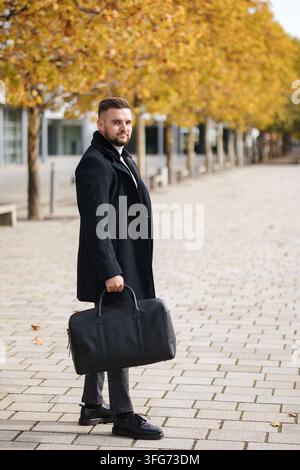Stylish businessman walking outdoors in an elegant coat, carrying a professional backpack on an autumn day. Warm fall colors, modern urban setting and Stock Photo