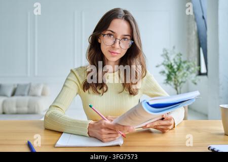 Smiling young female student sitting at desk during online video call Stock Photo