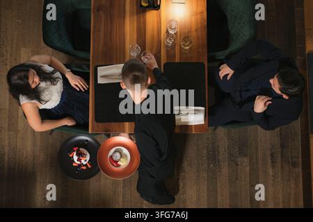 Waiter presents dessert to couple during fine dining experience in restaurant. They share a table and enjoy gourmet food. Stock Photo