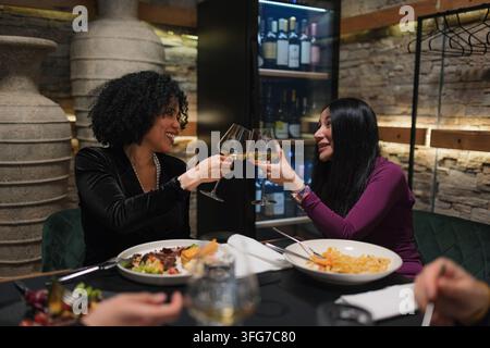 Two women celebrate their time together with a toast at a restaurant over dinner. They share joy and wine glasses. Stock Photo