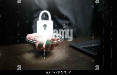 Cybersecurity concept. A man hand next to computer laptop in his office holding glowing padlock icon over working desk for system protection, security Stock Photo