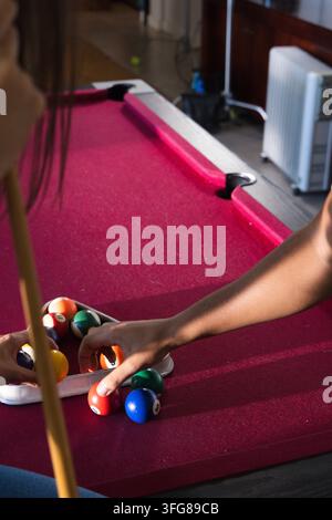 African American friends in casual tops arranging balls in triangle rack on red-felt table with cue Stock Photo
