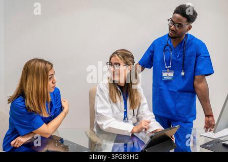 Medical team of doctor and nurses collaborating at a desk, using tablet and computer while discussing patient information, treatment plans and diagnos Stock Photo
