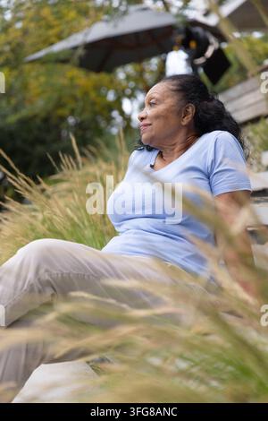 Senior African American woman sitting on stone step in backyard amid tall grasses Stock Photo