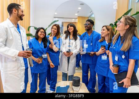 Diverse healthcare team of doctors and nurses smiling during a coffee break in a modern clinic, collaborating, exchanging ideas and showing teamwork a Stock Photo
