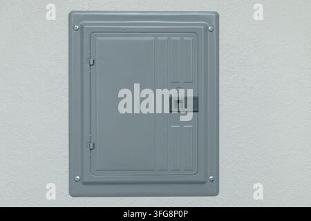 Gray metal electrical panel cover mounted on textured wall with screws, hinges, latch, and rectangular access door Stock Photo